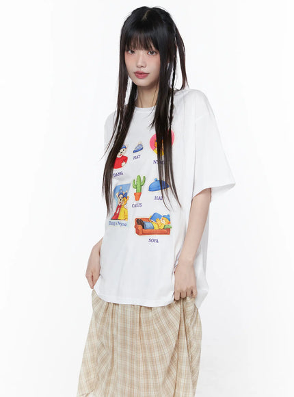 Oversized Graphic Print Tee CU519 in white, front three-quarter view on model, relaxed cotton short sleeve with vibrant cartoon character sticker graphics, paired with beige plaid midi skirt.
