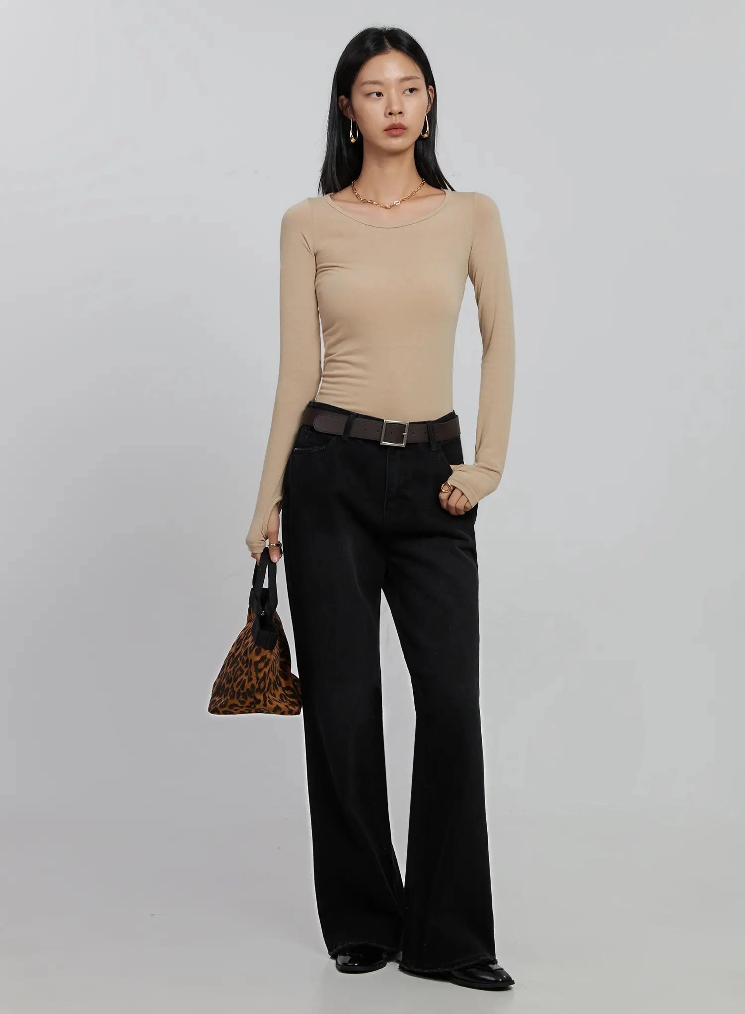 Imani Wide-Leg Flared Jeans ID516 in black, full-body front on model, styled with beige long-sleeve top, dark belt, and leopard print bag, long flared silhouette, minimal modern look.