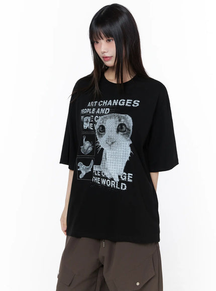 Oversized Cat Print Graphic Tee CU519 in black, front view on model, halftone cat collage graphic with 'Art Changes The World' slogan, relaxed drop-shoulder fit, paired with brown cargo pants.
