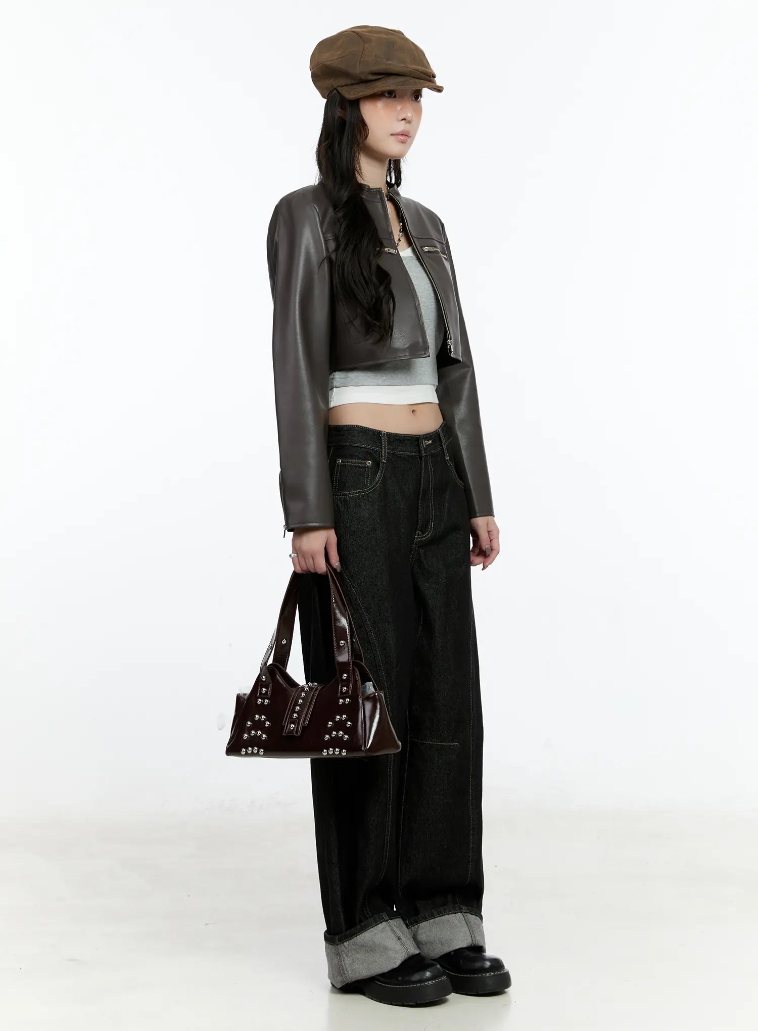 Maryam Low-Rise Dark-Washed Jeans CN517 in black, full-body side view on model, styled with brown cropped leather jacket, baker boy hat, and studded bag, cuffed hem detail.