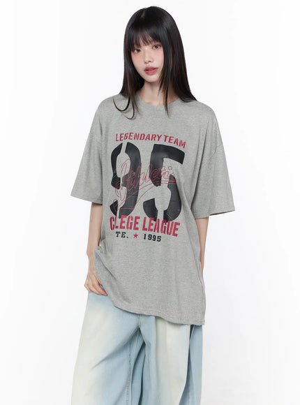 Oversized Graphic Tee CU519 in gray, front on model, relaxed drop-shoulder fit with bold Legendary Team 95 College League graphic, crew neck, paired with wide-leg light blue jeans.