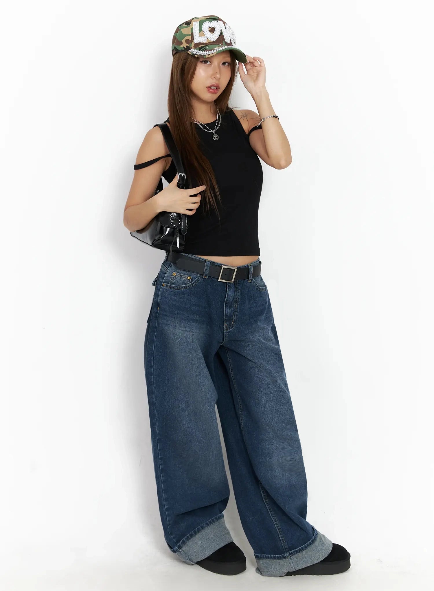 Anahi Baggy Jeans IN528 in blue, full-body editorial shot on model, belted low-rise wide fit paired with black crop top, camo cap, and black shoulder bag.