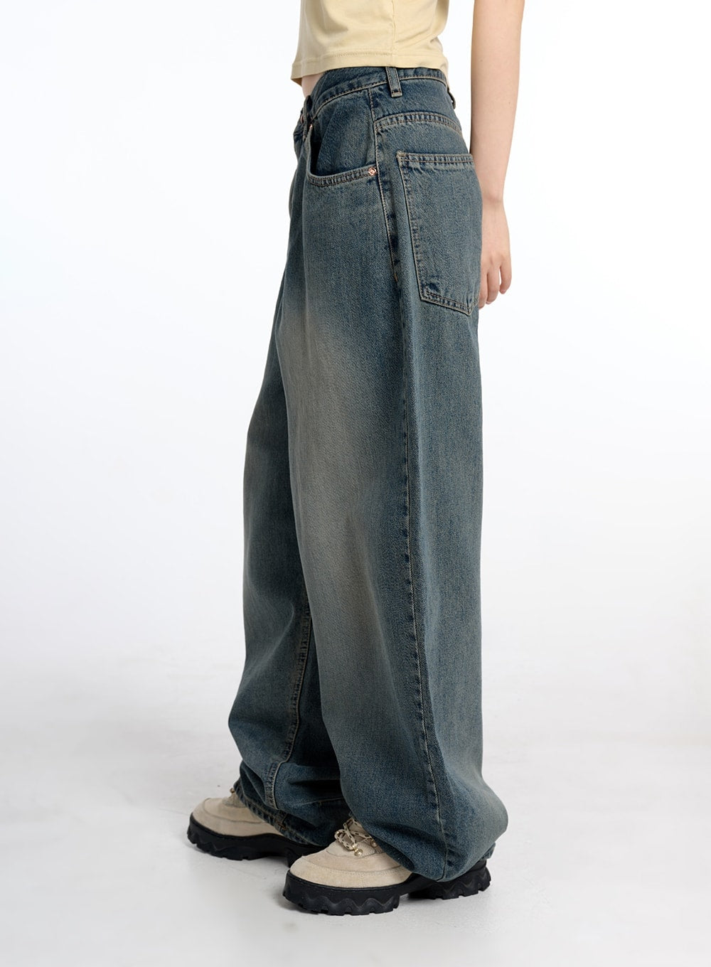 Vintage Low Rise Baggy Jeans CM415 in dark blue, side view on model, showing wide barrel-leg silhouette, back pocket detail, and vintage washed denim finish, styled with beige crop top and chunky sneakers.