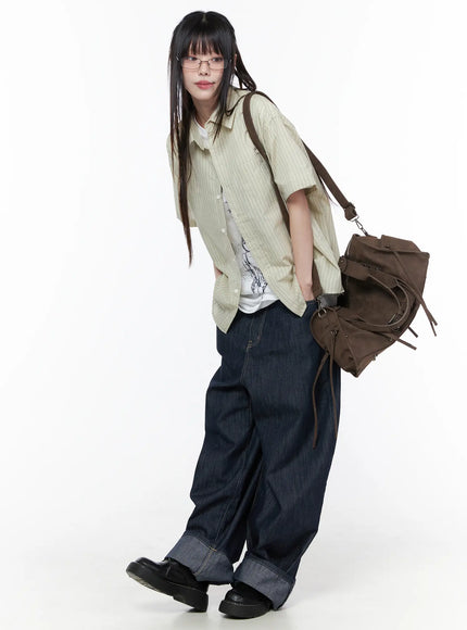 Rowen Baggy Jeans CU519 in dark blue, full-body editorial shot on model, styled with striped short-sleeve shirt and white tee, brown backpack, black loafers, casual Y2K look.