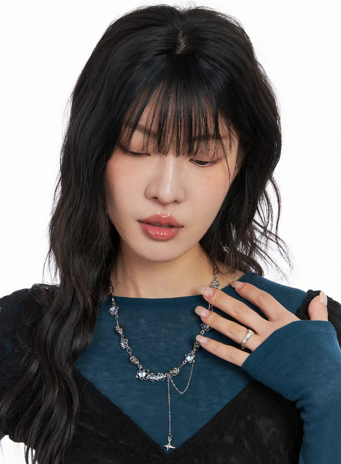 Blue Cubic Twist Necklace CC1809 in silver, front view on model looking down, glamorous K-pop style with iridescent blue beads, layered chain, and star pendant, paired with teal knit top.