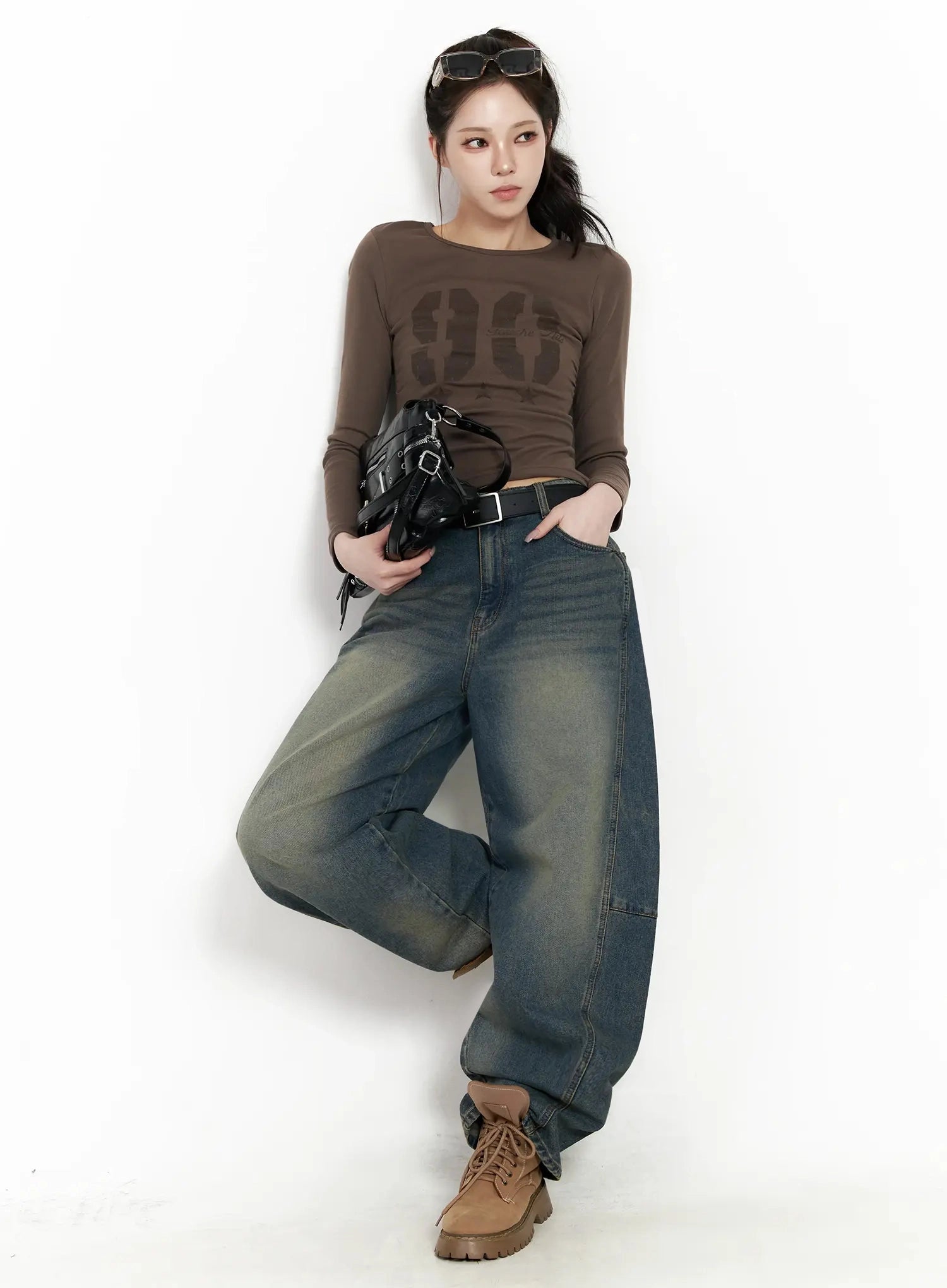Tata Vintage Dark Blue Washed Wide Leg Jeans IJ528 in dark blue, full-body editorial shot, model leaning against wall in relaxed pose, styled with brown graphic long-sleeve top, black bag, and tan boots.