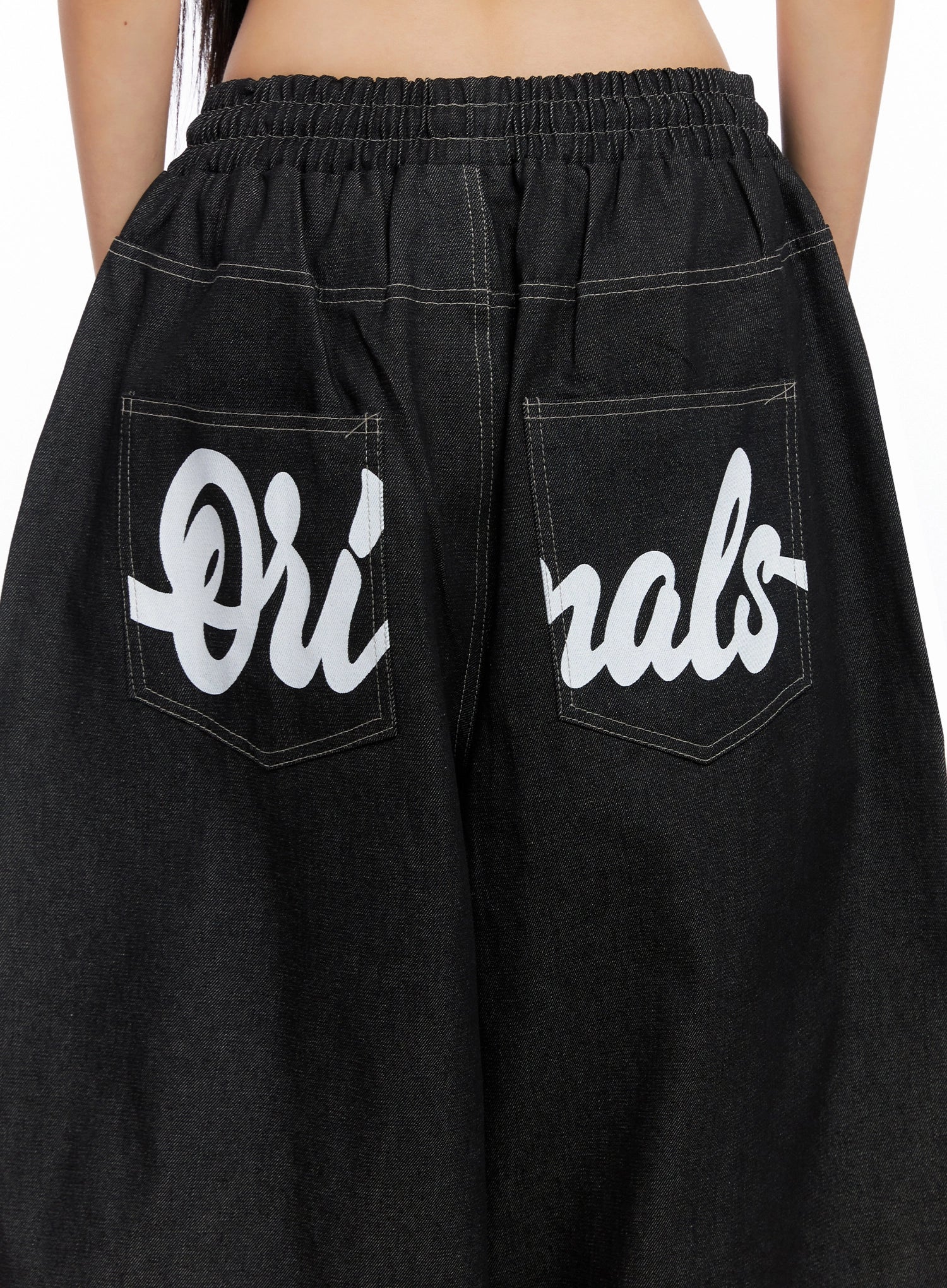 Ayra Graphic Baggy Jeans IO516 in Black, back close-up detail showing bold cursive Originals lettering across dual banded pockets, elastic waistband, and contrast white stitching.