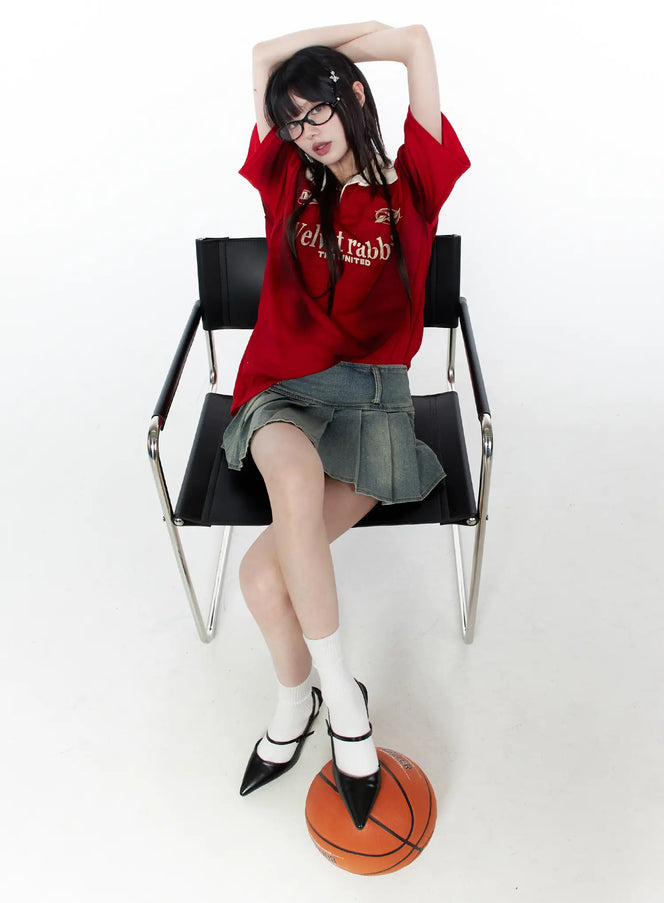 Oversized Collar Jersey CU519 in red, full-body seated on chair, oversized short sleeve with beige contrast collar and graphic print, styled with denim mini skirt, white socks, and heels, basketball at feet.