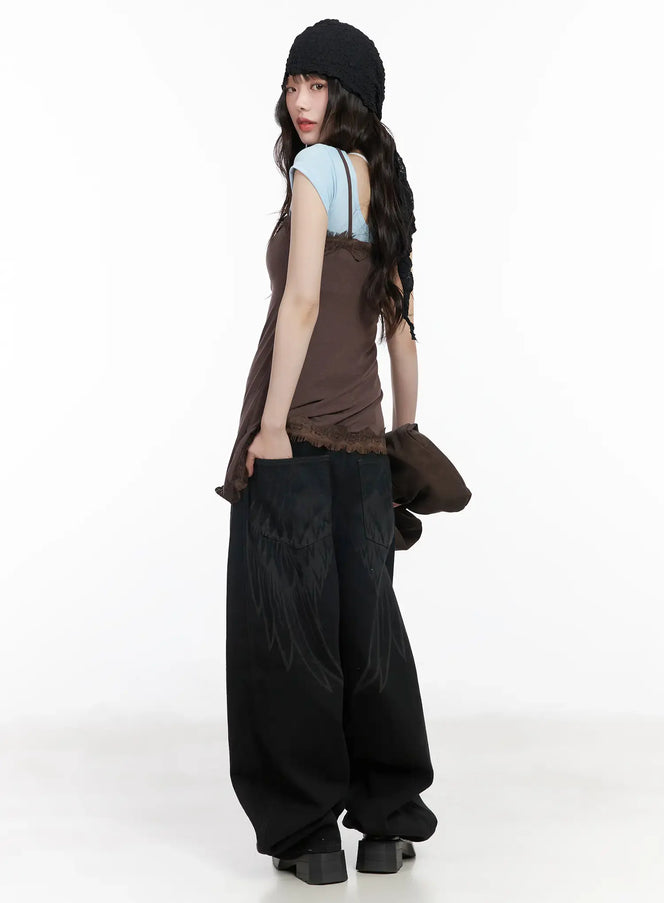 Angel Wing Wide-Leg Trousers CM526 in black, side-rear styled shot on model, full-length wide-leg silhouette with wing graphic, paired with brown cami, blue tee, and black beanie.