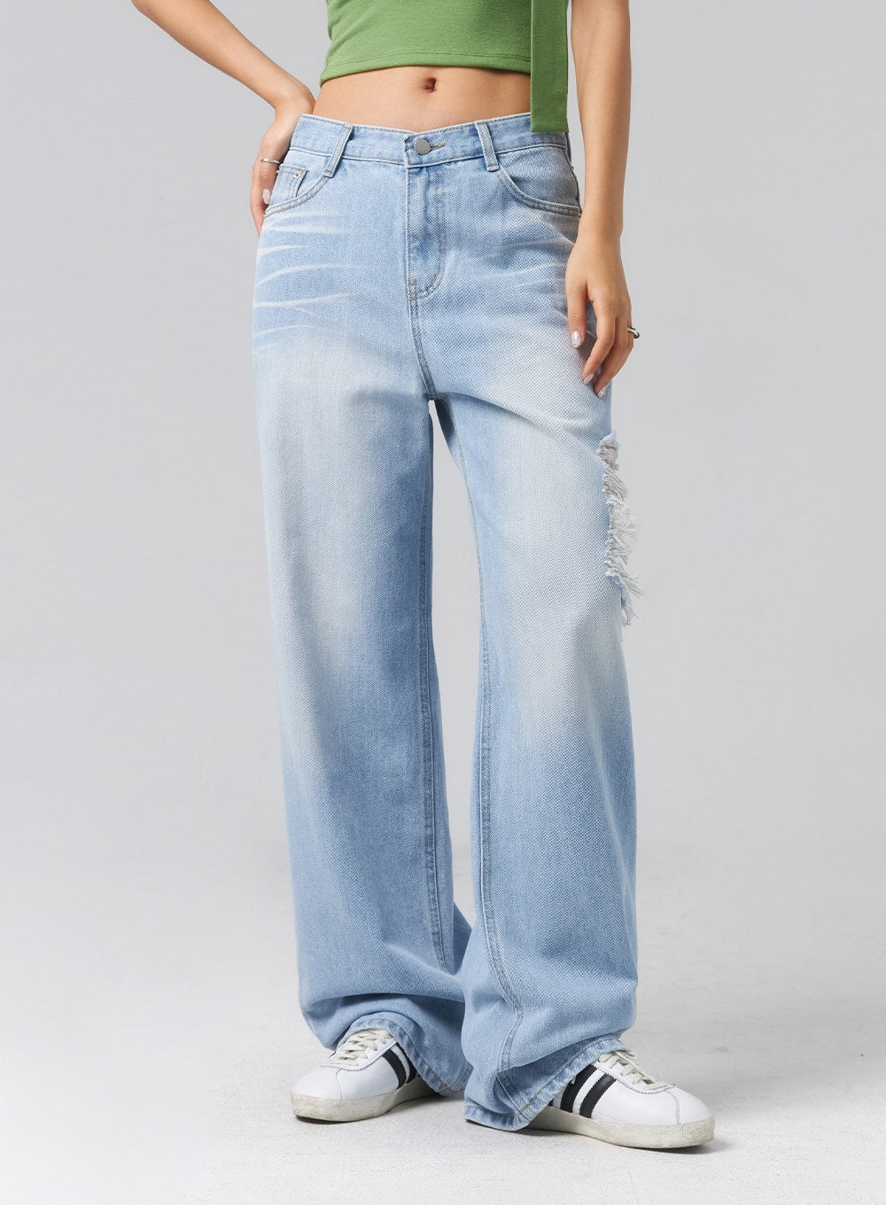 Ripped Side Jeans CL320 in light blue, front mid-shot on model, wide-leg cotton denim with faded wash and frayed destroyed detail visible at side thigh, paired with green crop top.