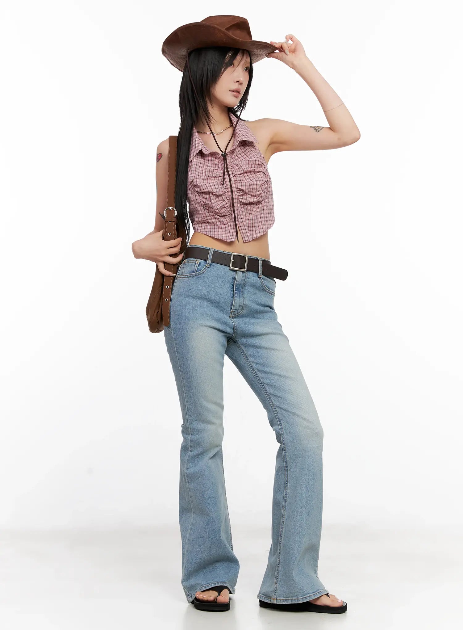 Byeol Washed Flare Denim Jeans CL525 in light blue, full-length angled shot on model styled with plaid crop halter top, brown belt, cowboy hat, and shoulder bag.
