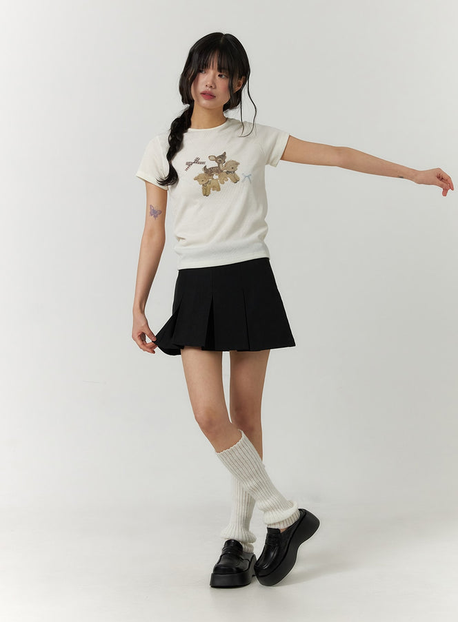 Pleated Mini Skirt CF407 in black, full-body front on model in dynamic pose, normal fit, styled with graphic tee, ribbed socks, and platform loafers.
