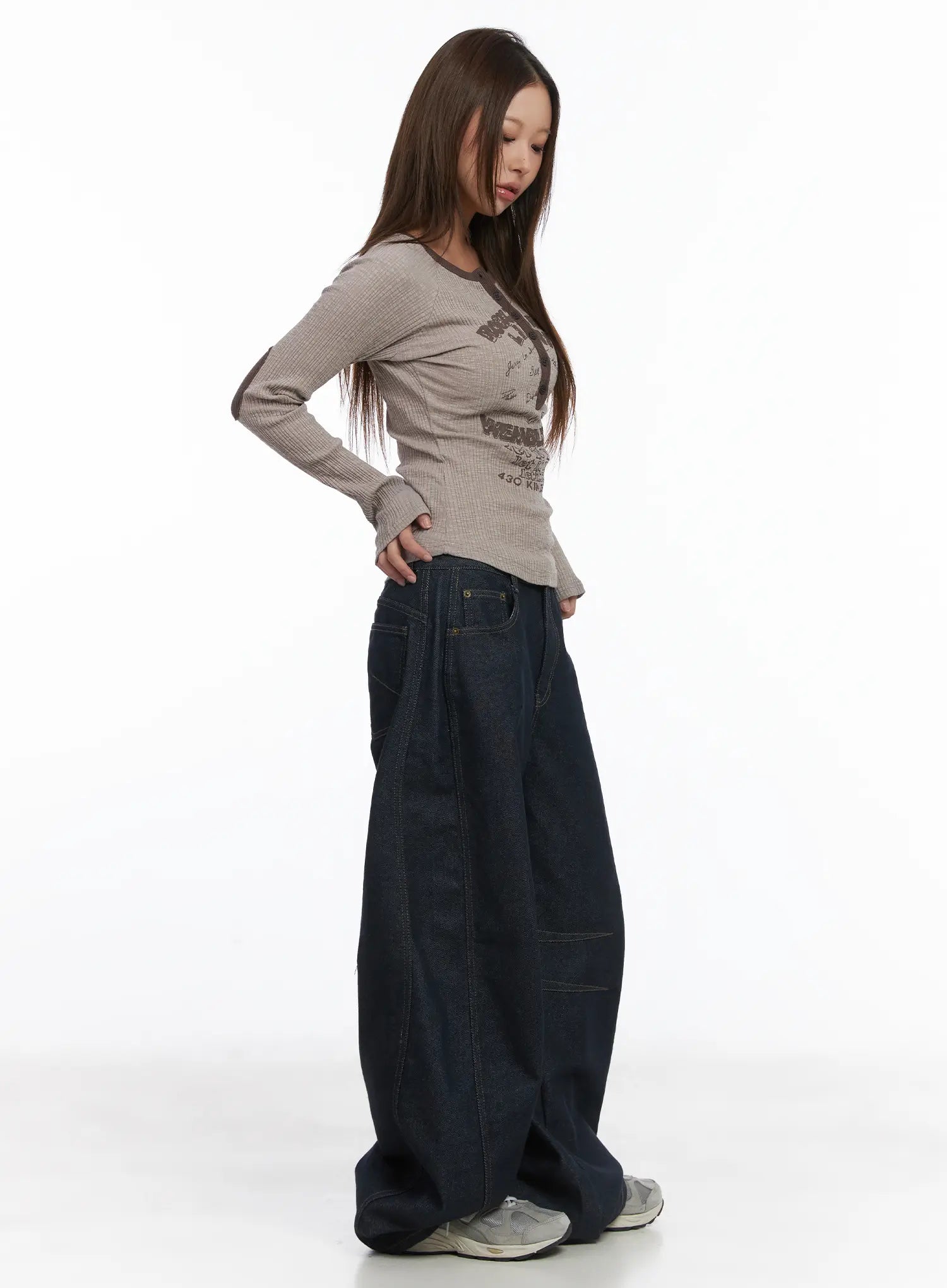 Mingyu Wide Jeans CJ512 in dark blue, side view on model looking down, showing exaggerated wide-leg balloon shape and long length pooling at sneakers, paired with graphic top.