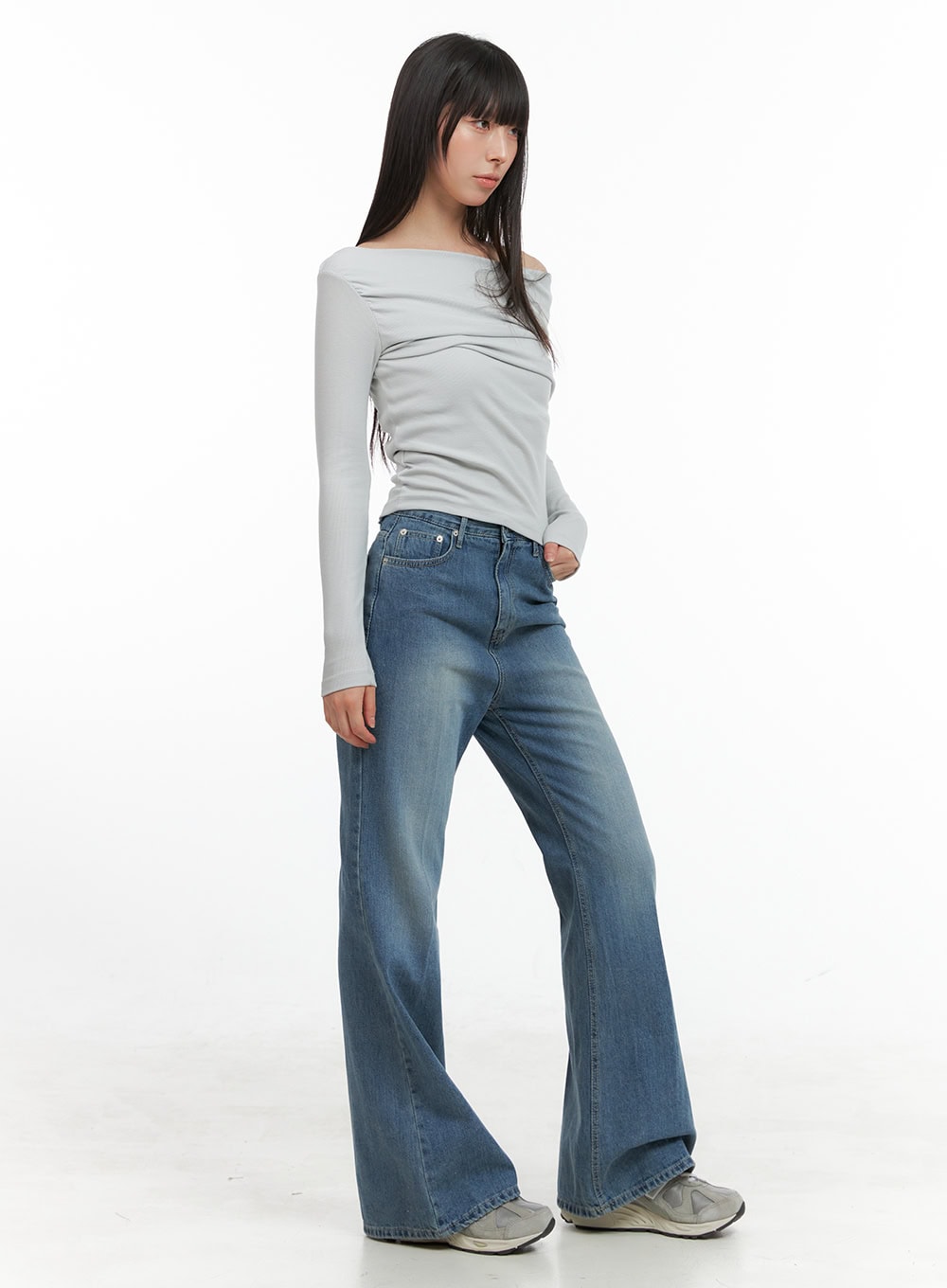 Daisy Loose Fit Bootcut Jeans CG419 in blue, side view on model, wide-fit flared washed denim showing silhouette and hem flare, with grey off-shoulder top and sneakers.