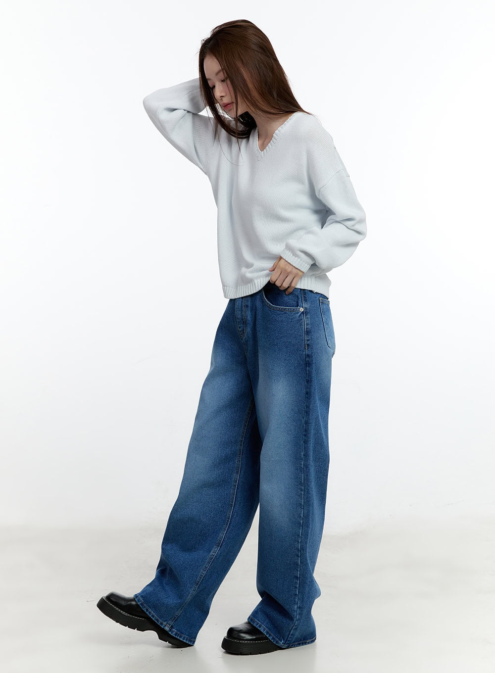 Eugene Adjustable Cinched-Back Wide-Leg Jeans CM521 in dark blue, three-quarter side shot on model in motion, wide-leg washed denim, paired with white V-neck knit and black platform shoes.