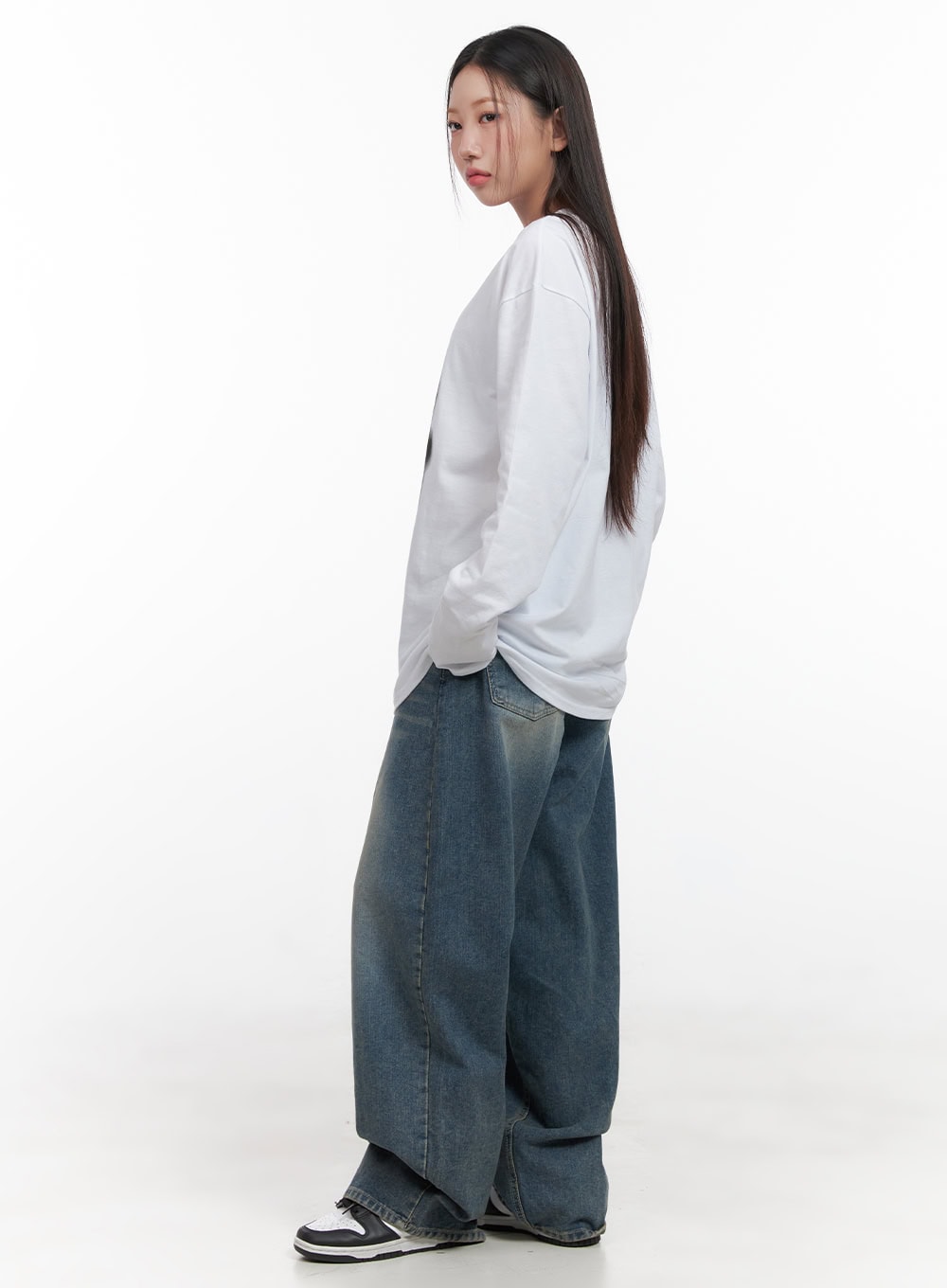 Mikaela Comfy Baggy Jeans CD411 in blue, side view on model turning away, wide-leg washed denim with voluminous silhouette, paired with white long-sleeve top and sneakers.