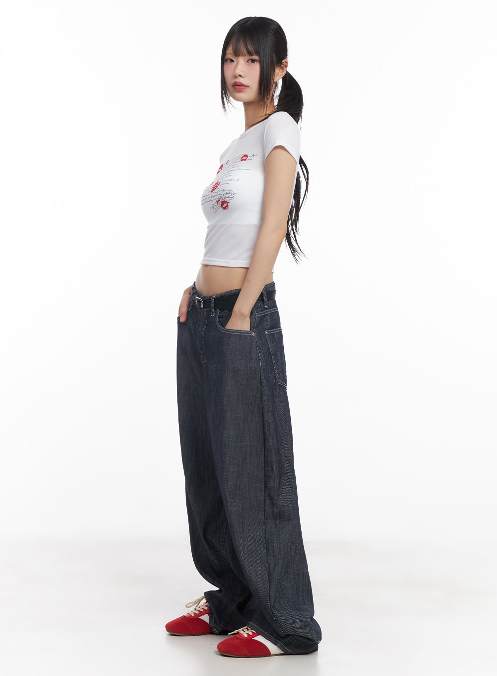 Isabel No-Fade Baggy Jeans CY514 in dark blue, side full-body shot on model, exaggerated balloon-leg silhouette, low-rise waistband with black belt, styled with white crop tee and red sneakers.