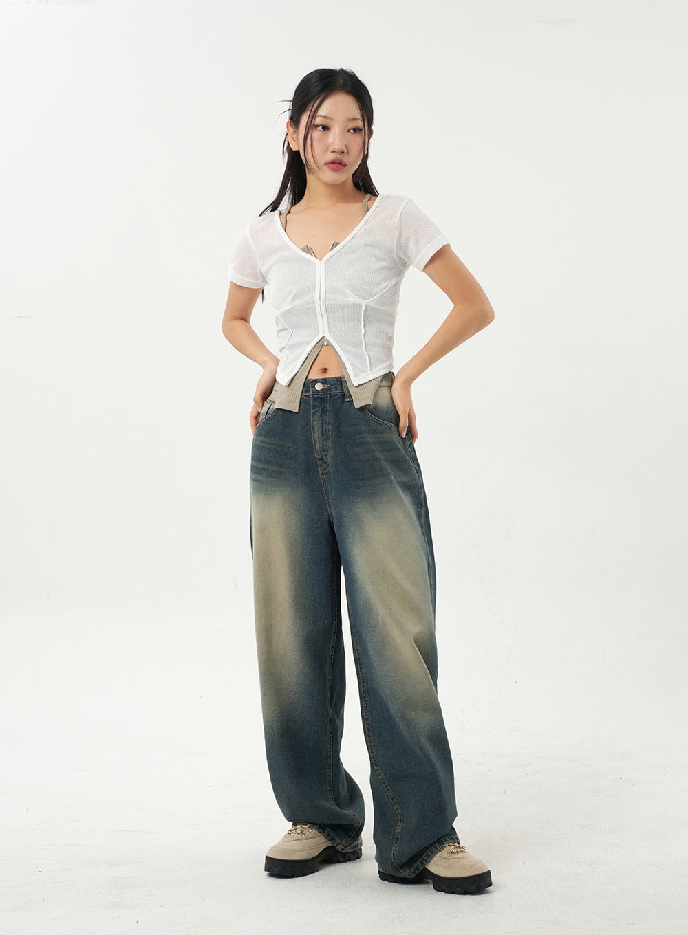 Mid-Rise Baggy Jeans CA325 in vintage blue denim, full-length front view on model with hands on hips, relaxed baggy fit and yellow-toned fading, styled with white sheer crop top and chunky boots.