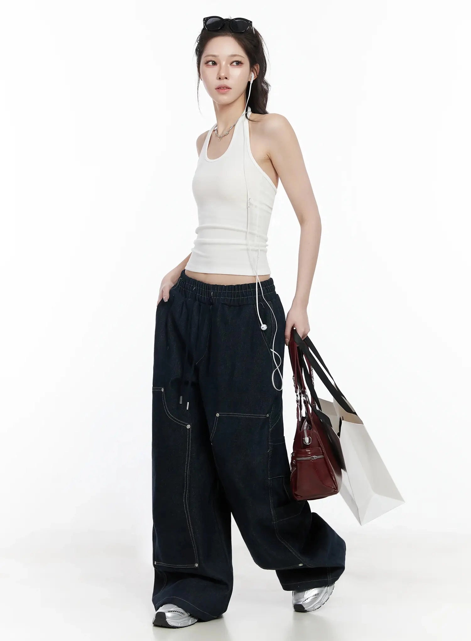 Ashlyn Carpenter Wide-Leg Jeans IJ528 in dark blue, three-quarter angle on model walking, paired with white halter top, carrying bags, drawstring waist and carpenter pockets visible.