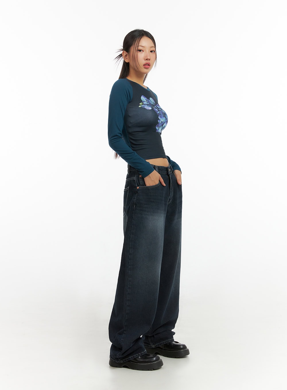 Evelyn Washed Baggy Jeans (Dark Blue) IS402 in dark blue, three-quarter side view on model, wide-fit washed cotton denim with subtle fading, paired with teal floral long-sleeve crop top.