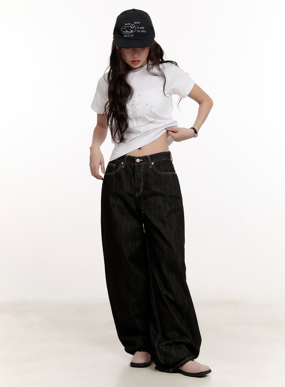 Trinity Stitched Baggy Jeans CM510 in black, full-body front view on model, wide-fit low-rise denim with contrast stitching, styled with white crop tee and black cap.
