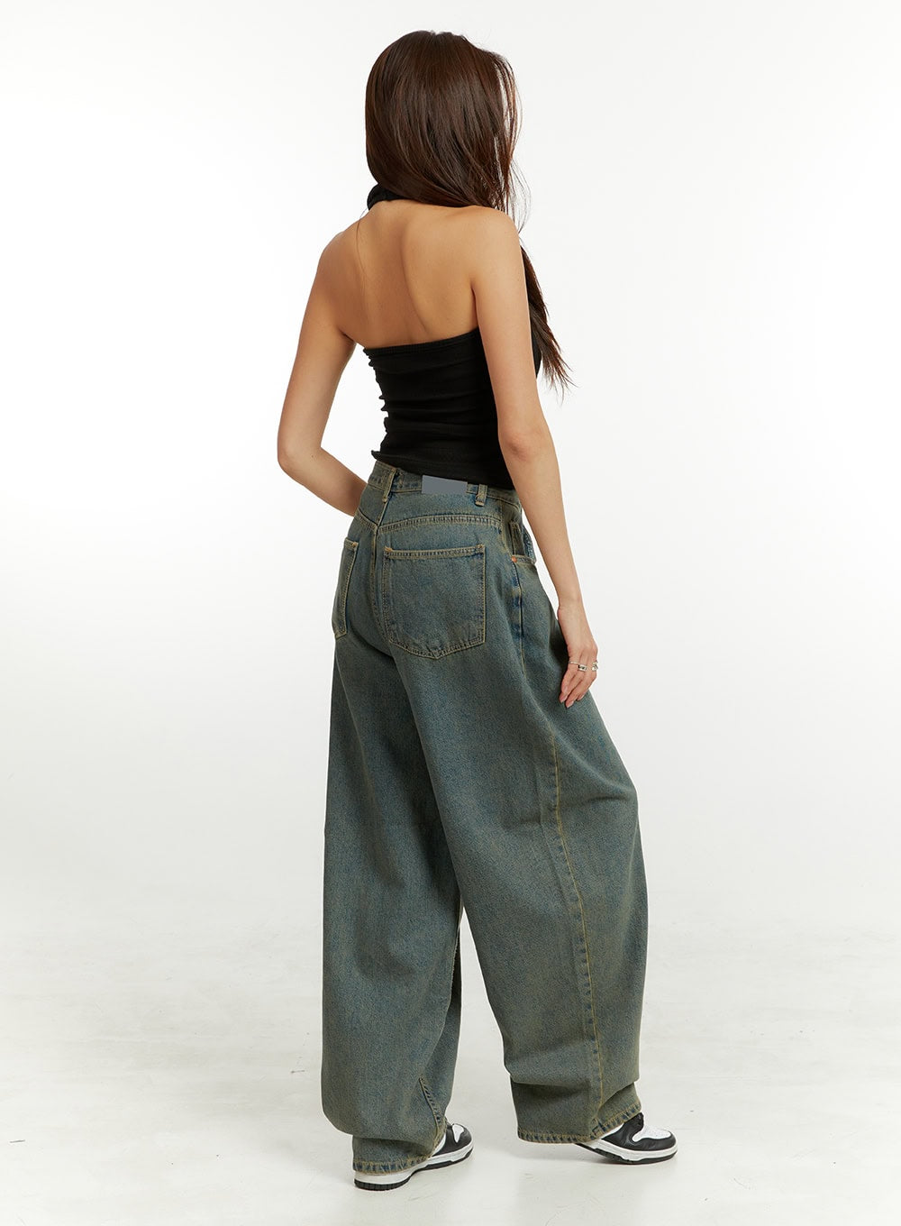 Denim Washed Baggy Jeans CU424 in blue, back three-quarter view on model, showing curved wide-leg silhouette and washed denim texture, paired with black halter top and sneakers.