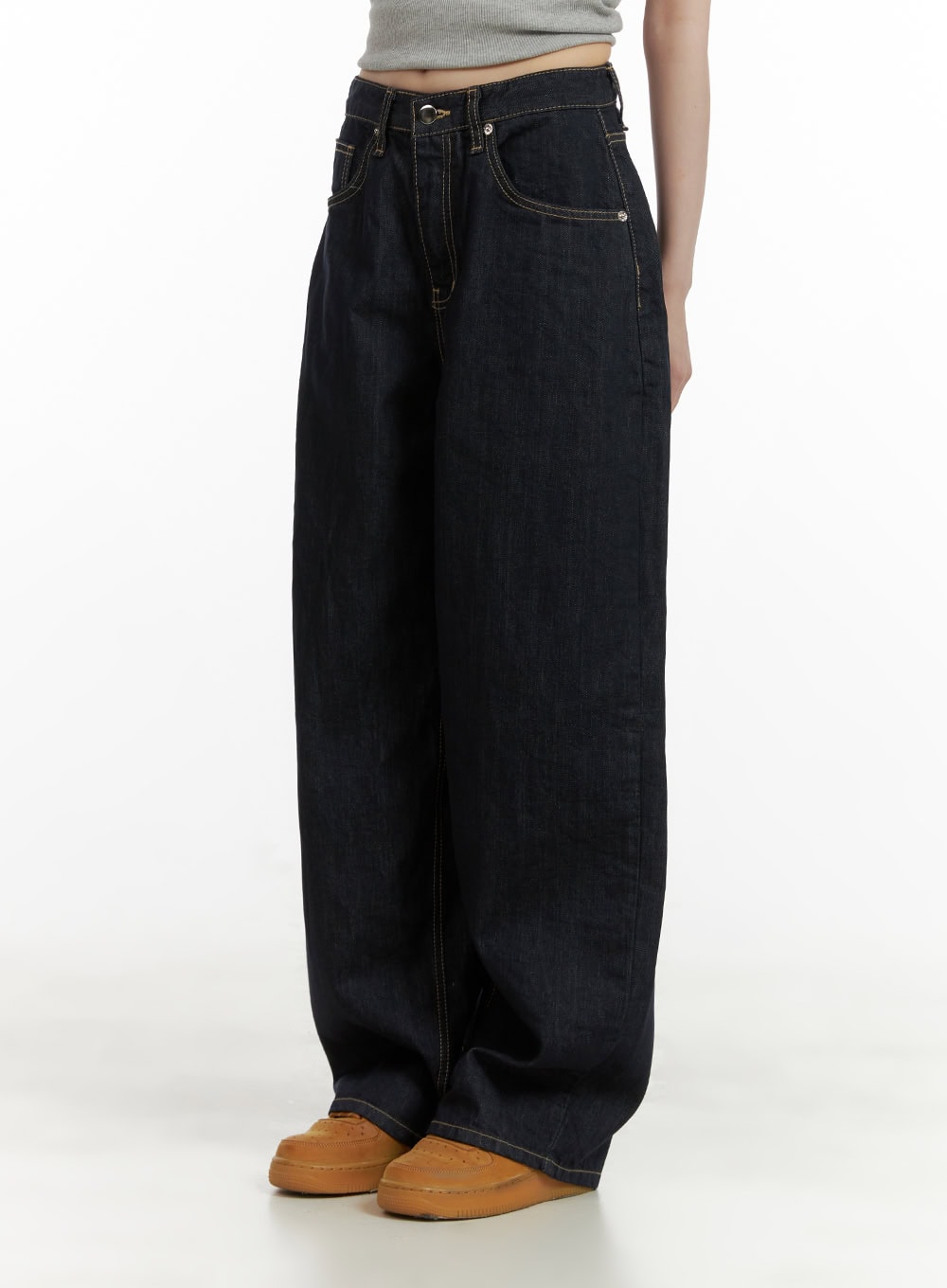 Stitch Detail Baggy Jeans CU410 in dark blue, side view on model, wide-fit denim showing contrast topstitching and roomy leg opening, paired with grey crop top and tan sneakers.