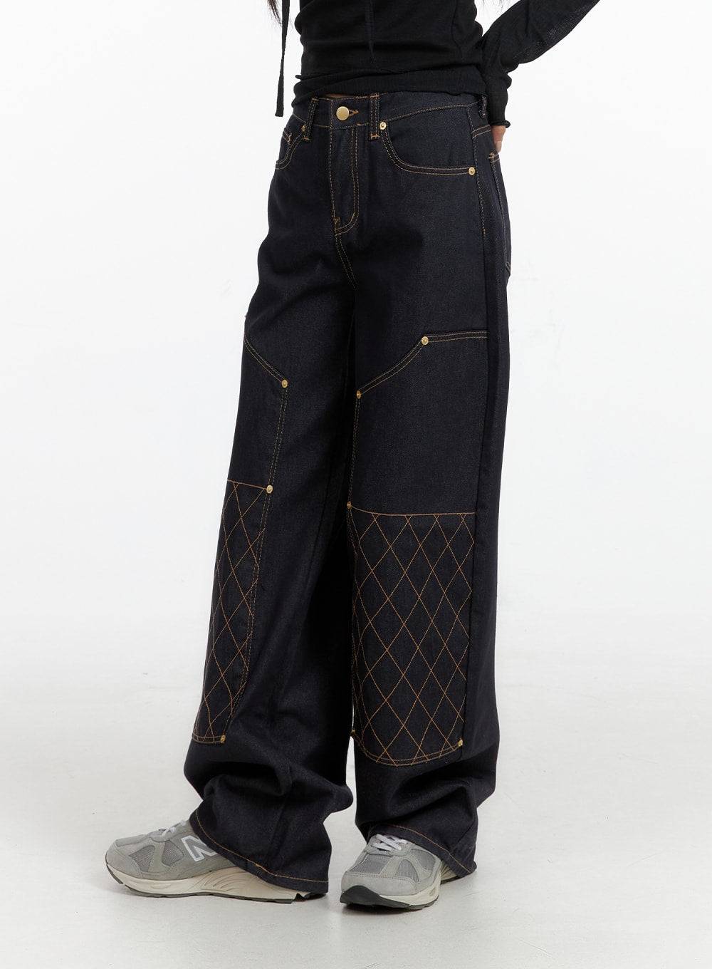 Stitched Wide Denim Jeans CF408 in dark navy, side view on model, showing panelled construction with contrast amber topstitching and diamond quilt detail on lower leg, worn with grey sneakers.