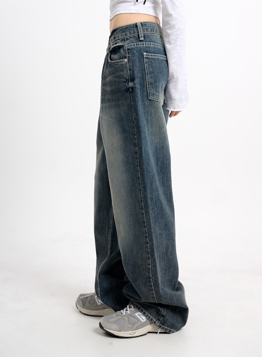 Low Waist Baggy Jeans CM415 in dark blue, side view on model, showing extra-wide leg and washed denim texture with contrast stitching, paired with grey crop top and sneakers.