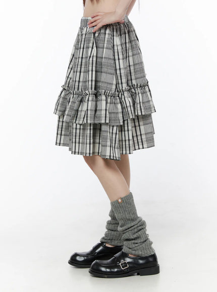 Plaid Layered Midi Skirt CU519 in black, side view on model, showcasing two gathered ruffle tiers and volume silhouette, black-white plaid fabric, with grey leg warmers and loafers.