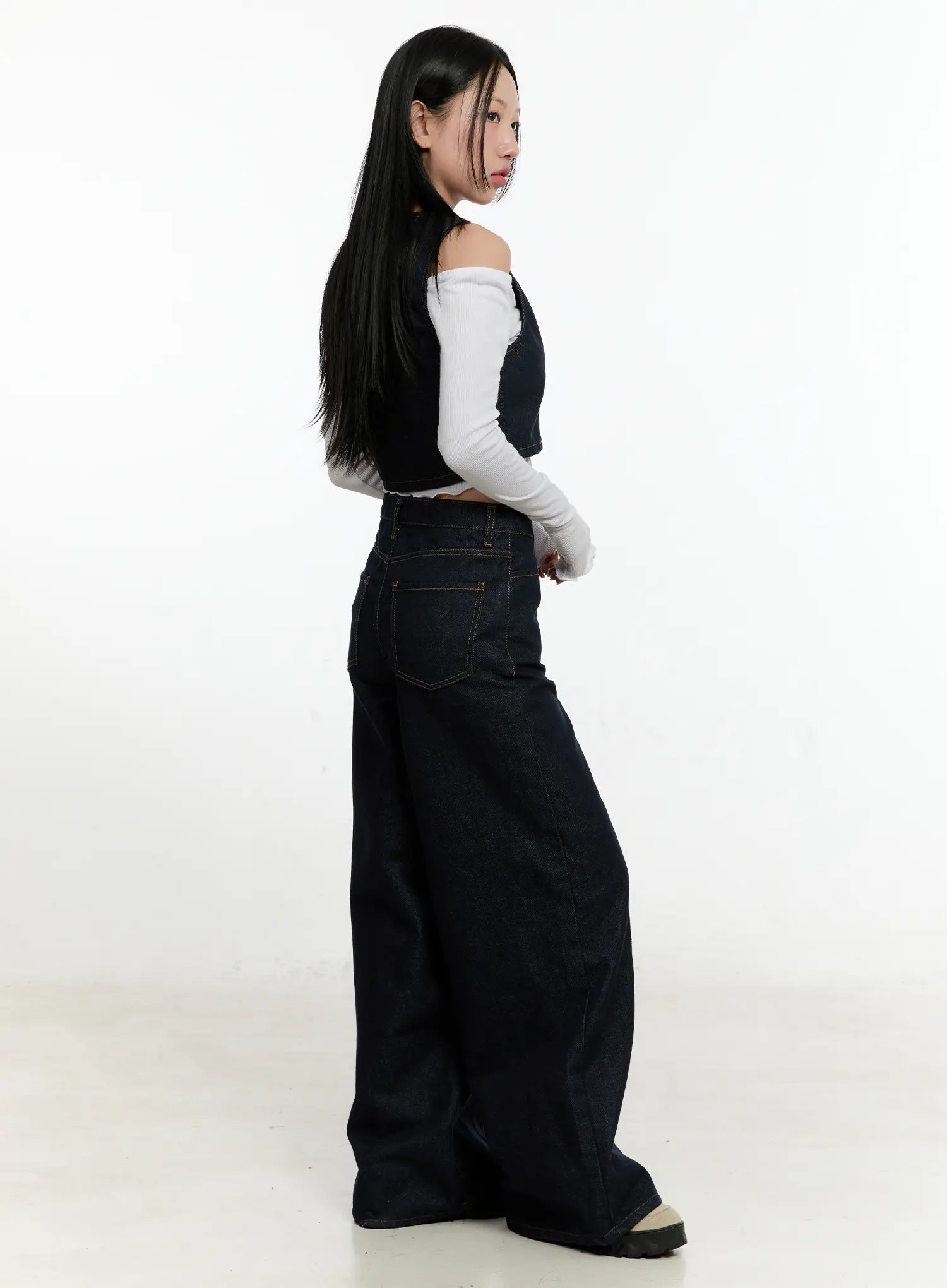 Nala Wide-Leg Bootcut Jeans CN506 in dark blue, side-back view on model glancing over shoulder, back pocket and sweeping wide leg visible, styled with denim vest.