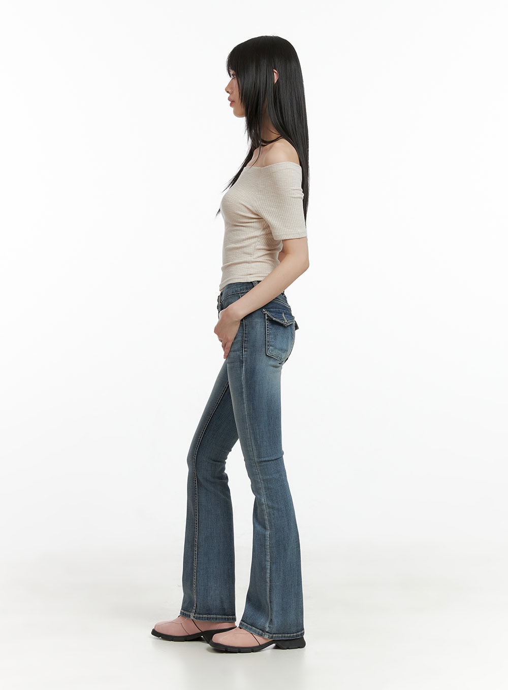 Tight Fit Low Waist Bootcut Jeans CL403 in dark blue, side view on model, slim through hip with flared hem, washed denim, paired with beige off-shoulder top and pink mules.