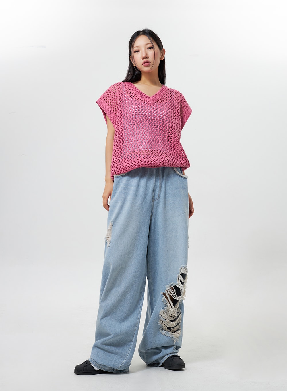 Oversized Ripped Jeans CY324 in light blue, full-body front view on model, relaxed wide-fit denim with ripped knee detail, paired with pink open-knit vest, casual street style.