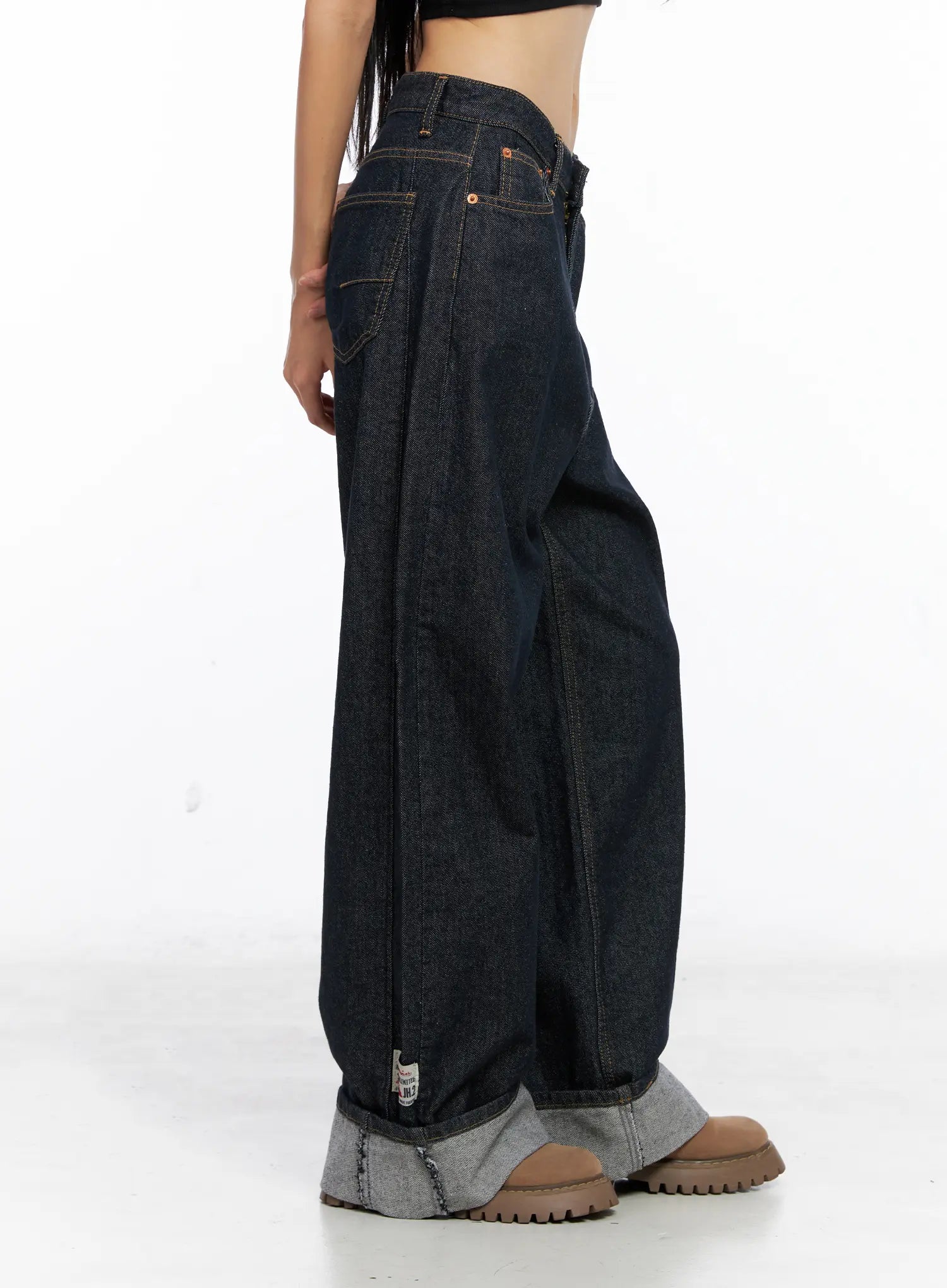 Oakley Cuffed Wide-Leg Jeans CS511 in dark blue, side view on model, showing loose cotton silhouette, contrast grey rolled cuff at hem, side seam stitching, and patch label at ankle.