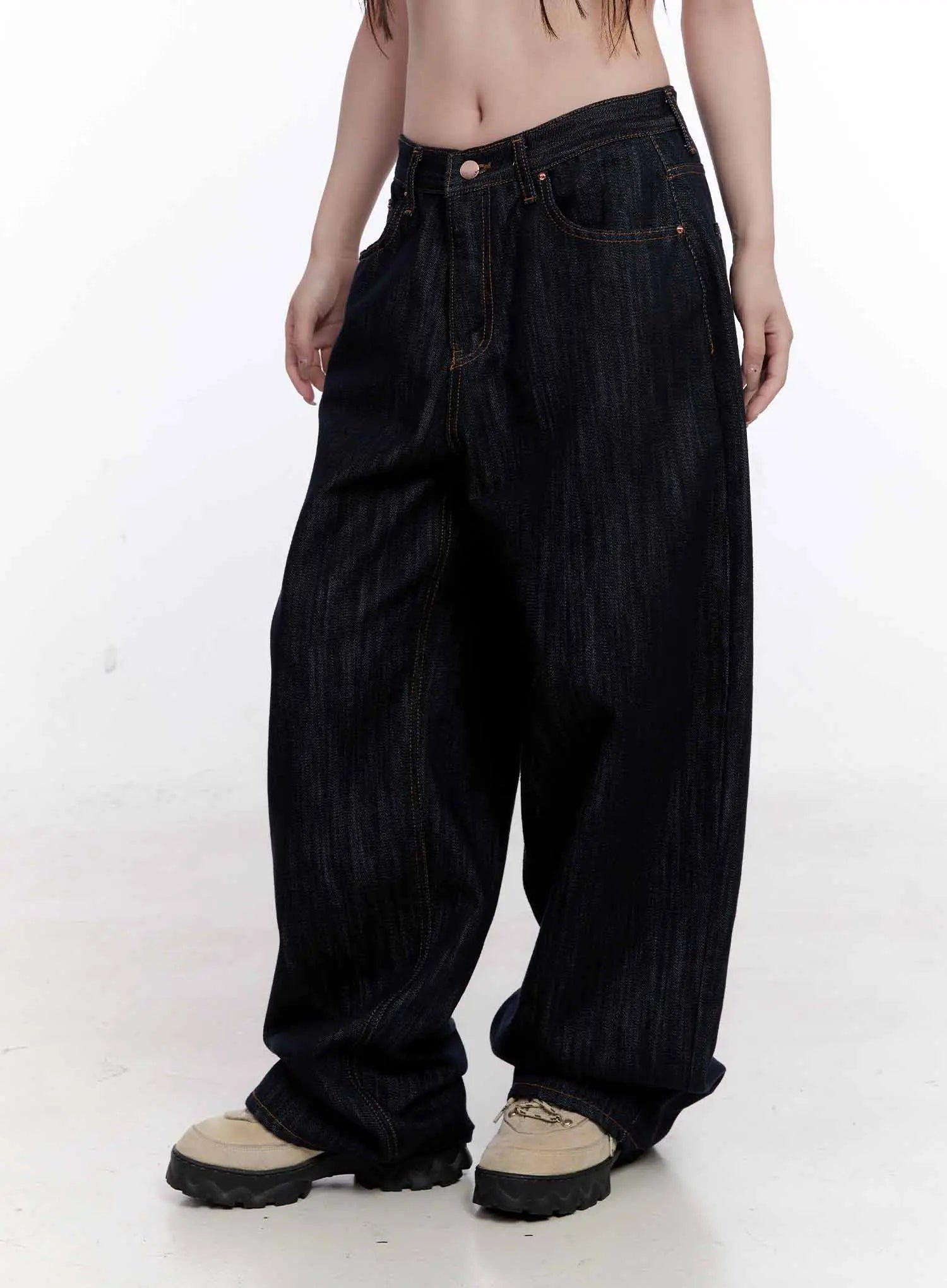 Haewon Dark Washed Baggy Jeans CS530 in dark blue, front mid-body view on model, arms at sides, low-rise waistband with copper rivets, voluminous baggy leg silhouette in cotton denim.