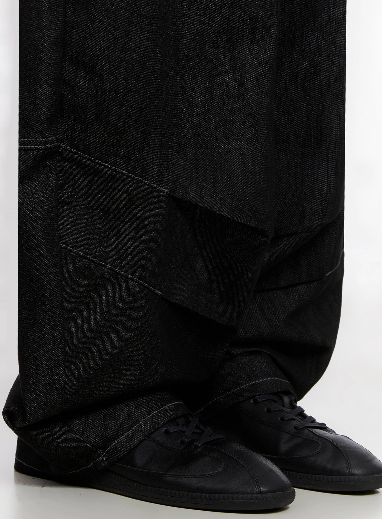 Leyla Pin-Tuck Wide-Leg Jeans IS515 in black, close-up of hem detail, layered pintuck panel at lower leg pooling over black sneakers, contrast stitching visible.