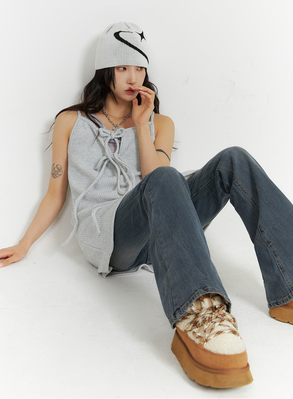 Slim Washed Flared Jeans CF416 in mid-blue, seated side pose on model, flared leg silhouette visible, paired with grey lace-up tank and logo beanie.