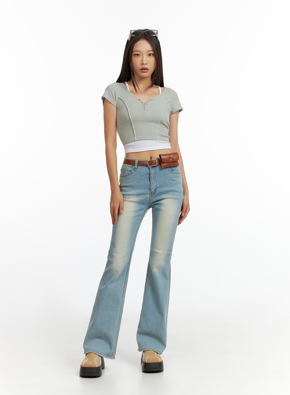 Light Washed Slim Fit Bootcut Jeans IL409 in light blue, front standing shot on model, high-rise waist with belt, bootcut flare hem, styled with grey crop top and fanny pack.