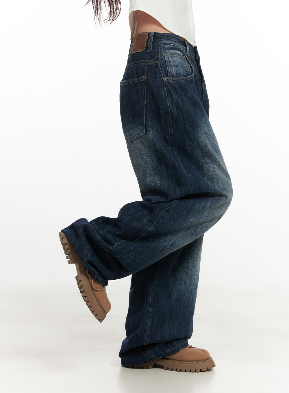 Jessica Wide-Fit Denim Jeans CN426 in blue, side close-up on model mid-stride, showing extreme wide-leg volume, back leather patch tab, washed denim with fading, styled with chunky shoes.