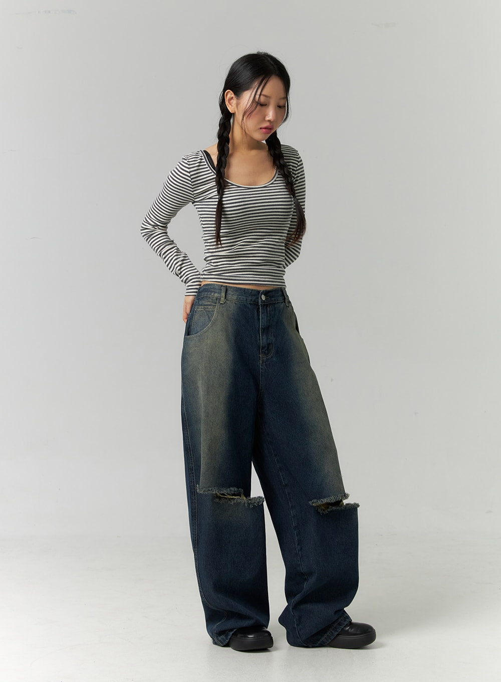 Destroyed Washed Wide Leg Jeans CN324 in dark blue, front angle view on model looking down, low-rise waist with button fly, oversized wide leg pooling at hem, frayed ripped knees, paired with striped top.