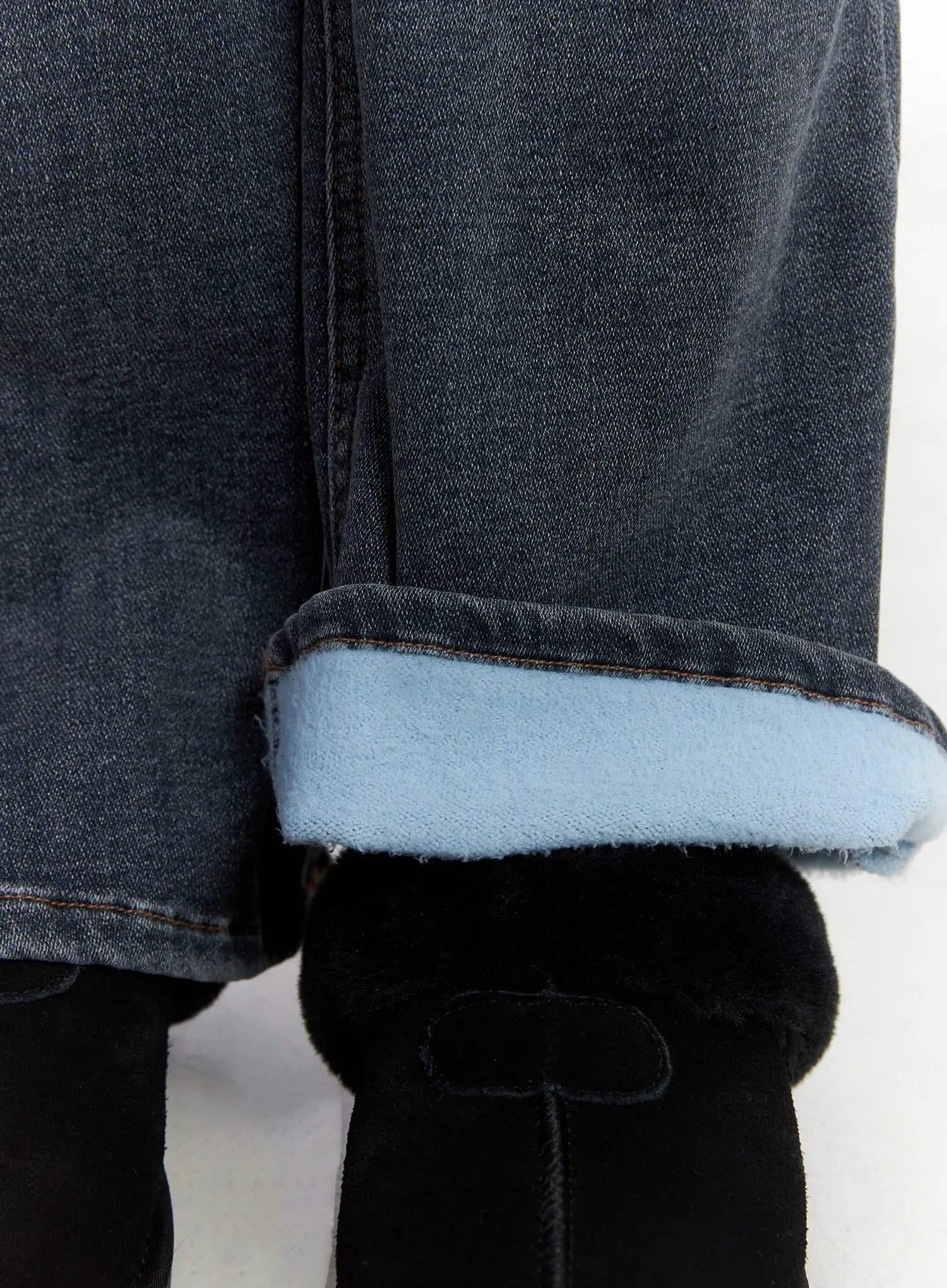 Kiera Low-Rise Fleece-Lined Bootcut Jeans CD509 in washed dark blue, close-up of bootcut hem revealing light blue fleece inner lining, worn over black shearling boots.