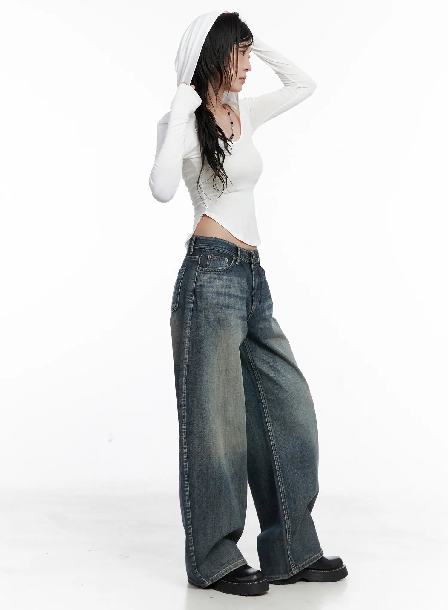 Nellie Baggy Jeans CS526 in blue, side angle on model mid-pose, washed baggy denim with low waist and curved wide leg, paired with white hooded crop top.