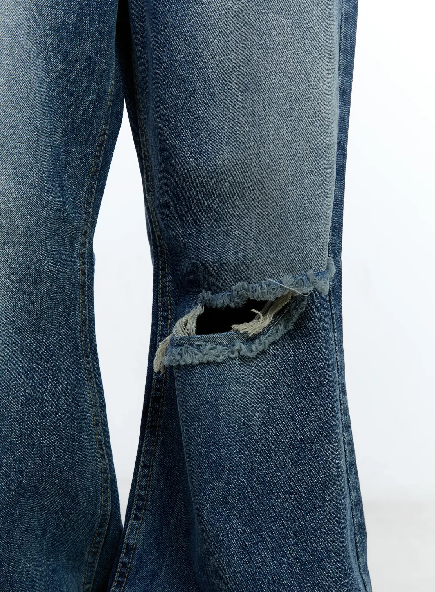 Gabi Distressed Semi-Flared Denim Jeans CG501 in dark blue, macro close-up of knee rip detail showing frayed edges and semi-flare seam on washed cotton denim.