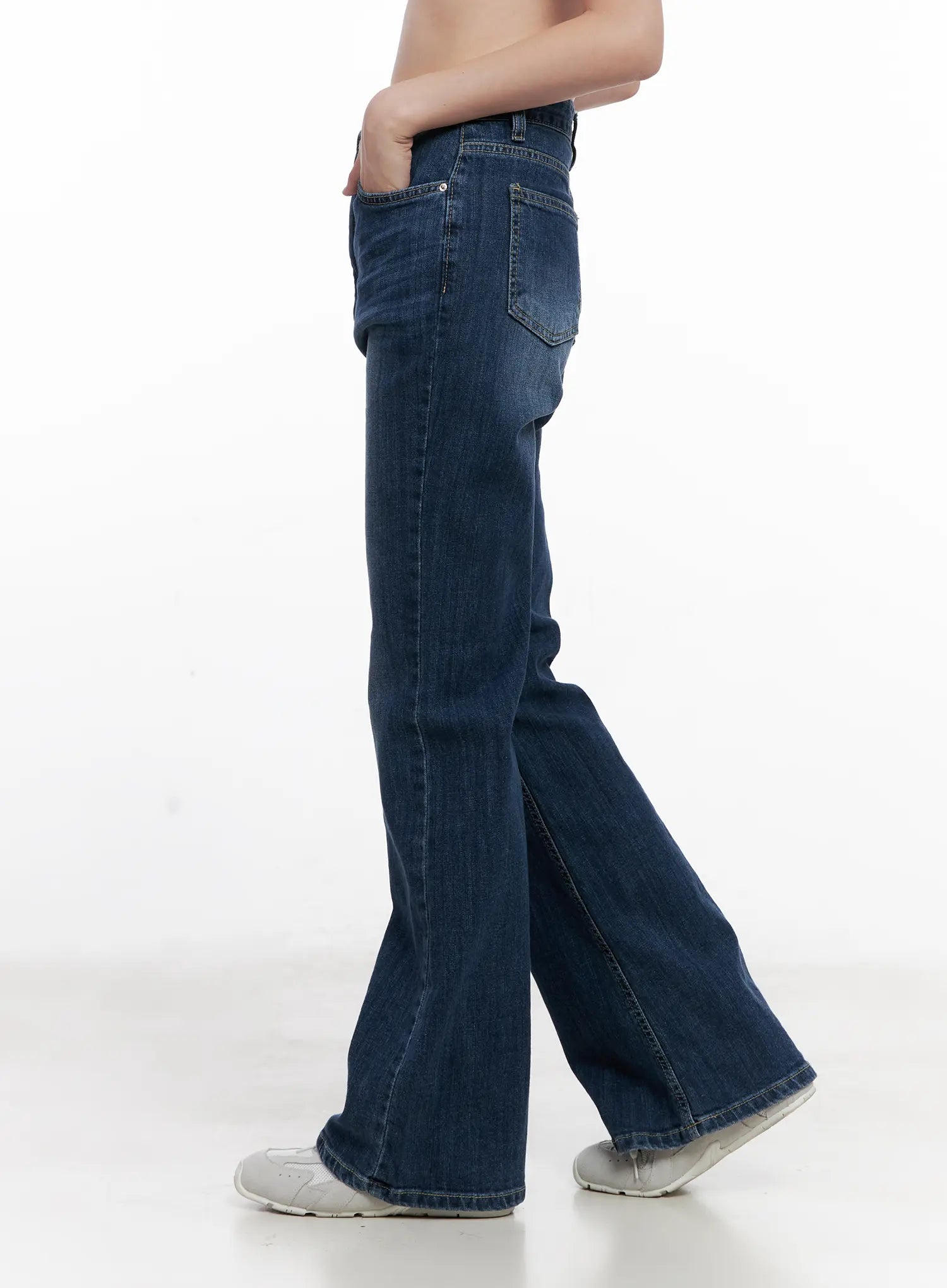Solhee Classic Flare Denim Jeans CL524 in dark blue, side view on model, showing flare hem sweep, back pocket detail, washed denim texture, paired with white sneakers.