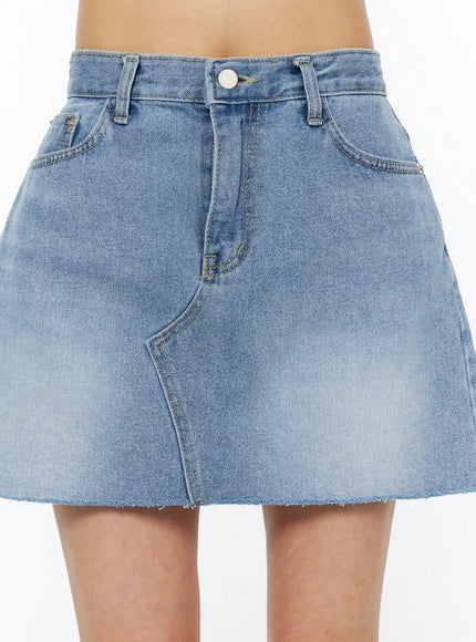 Casual Denim Mini Skirt CU522 in light blue, front close-up detail shot, showing button closure, belt loops, side pockets, curved seam, and frayed raw hem.