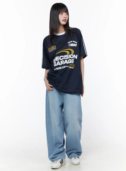 Oversized Sporty Graphic Tee CU519 in dark blue, full-body front on model, mesh oversized silhouette with white sleeve stripes and racing graphic, styled with wide-leg jeans and sneakers.