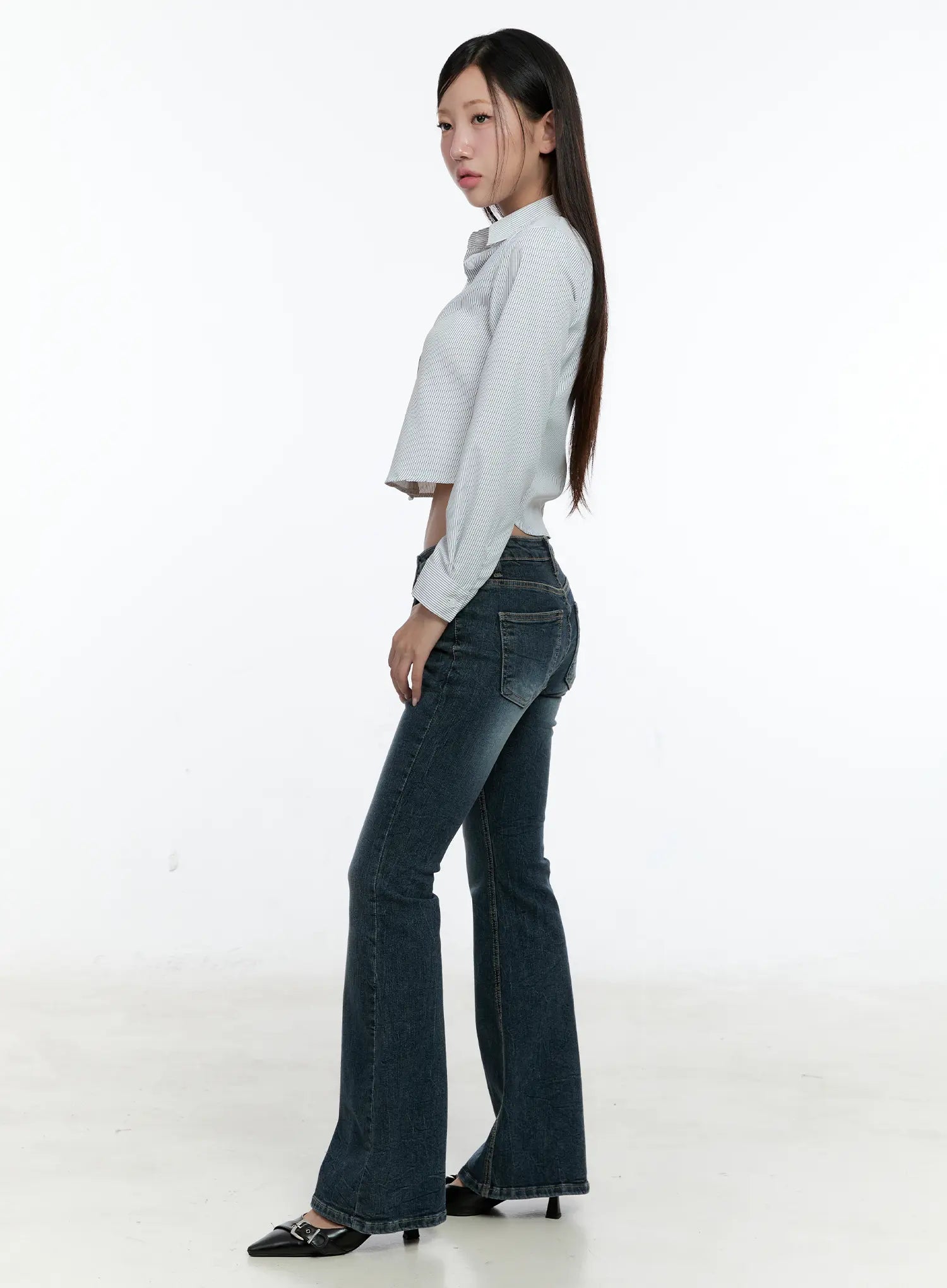 Harlee Bootcut Jeans CS517 in dark blue, side view on model glancing back, showing slim fit through thigh flaring into bootcut hem, paired with a cropped white stripe shirt and black heels.