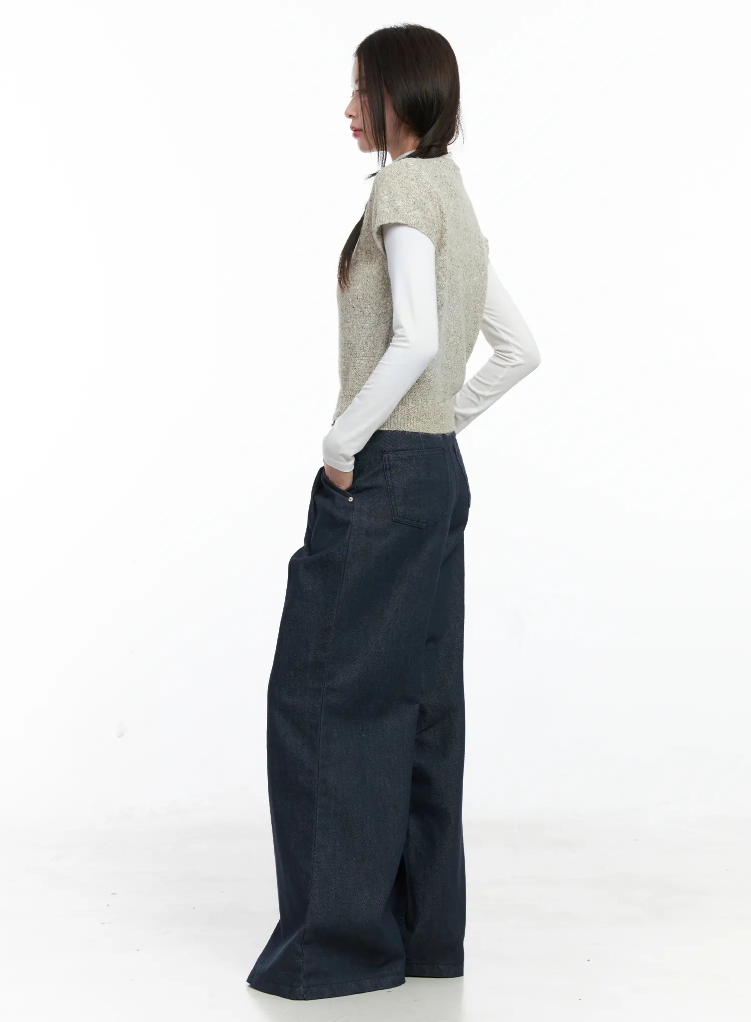Lena Pintuck Baggy Jeans CO503 in dark blue, three-quarter back-side view on model, showing long wide flared leg and back patch pockets, styled with beige knit vest and white turtleneck.