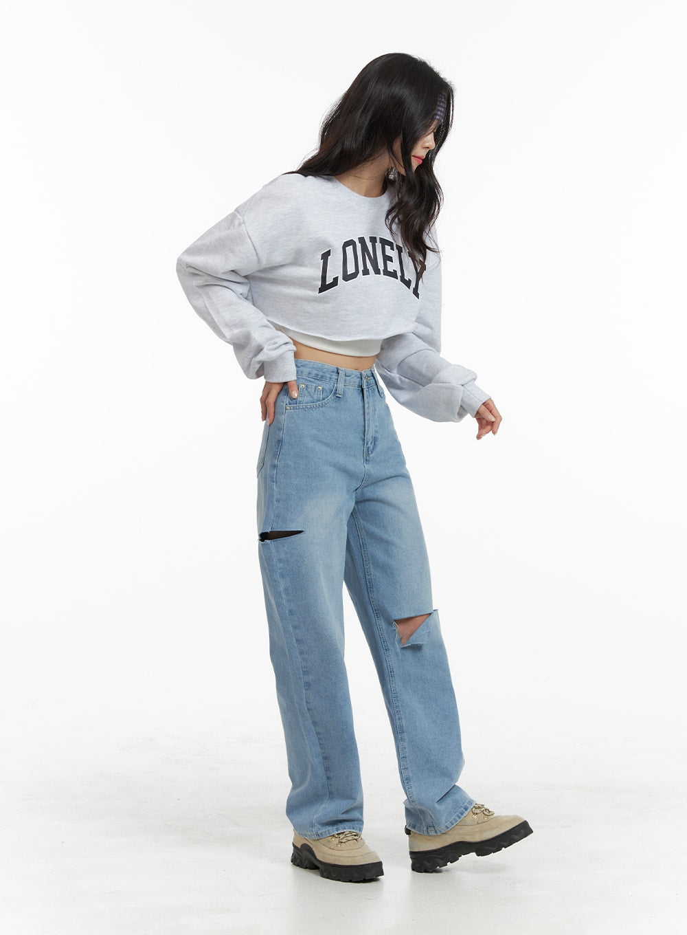 Cut Out Washed Straight Jeans OM421 in blue, three-quarter back-angle on model looking down, thigh cut-out detail visible on side, paired with grey crop sweatshirt and chunky shoes.