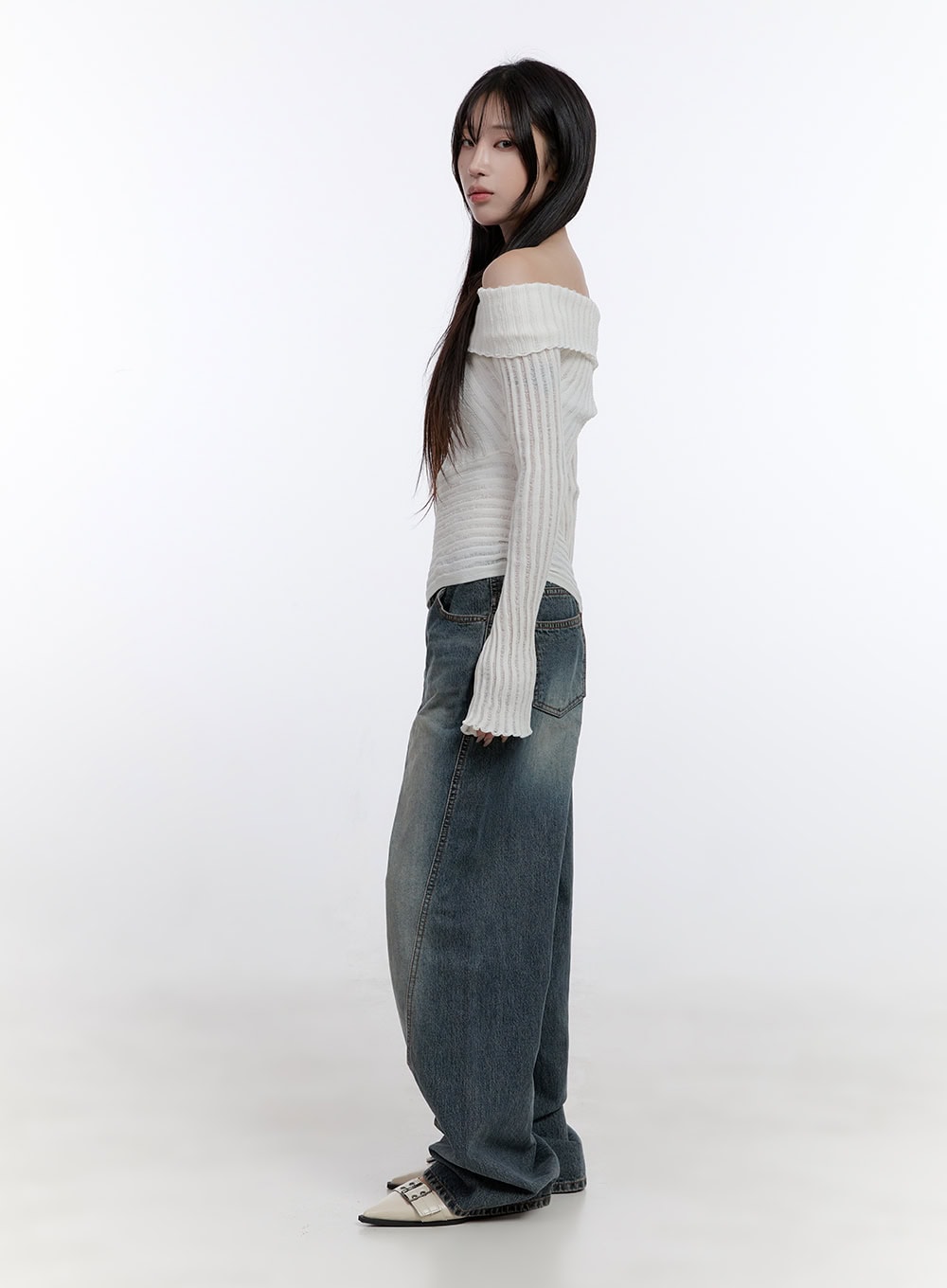 Lucia Stitched Denim Baggy Jeans CO418 in blue, side full-body view on model, showing wide-leg silhouette and curved panel stitch, paired with off-shoulder cream knit top.